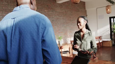 Smiling-african-american-woman-paying-male-barista-by-credit-card-at-coffee-shop,-slow-motion