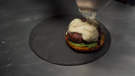 chef at gourmet restaurant melt cheese over premium sirloin tenderloin meat for hamburger over stone plate hot raclette