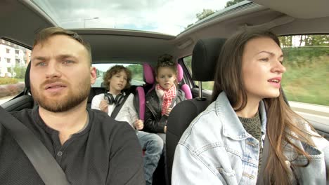 front view of happy loving parents and their excited kids smiling driving a car in the city. young family traveling abroad by auto