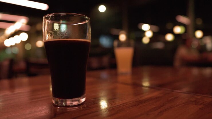 Una pinta di stout scura è appoggiata su un tavolo da bar in legno con luci bokeh sullo sfondo