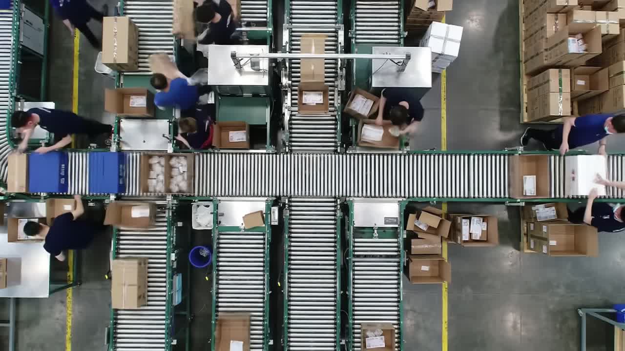 Efficient Packaging Operation in a Modern Warehouse: Aerial View of Employees Sorting and Moving Parcels on a Conveyor System