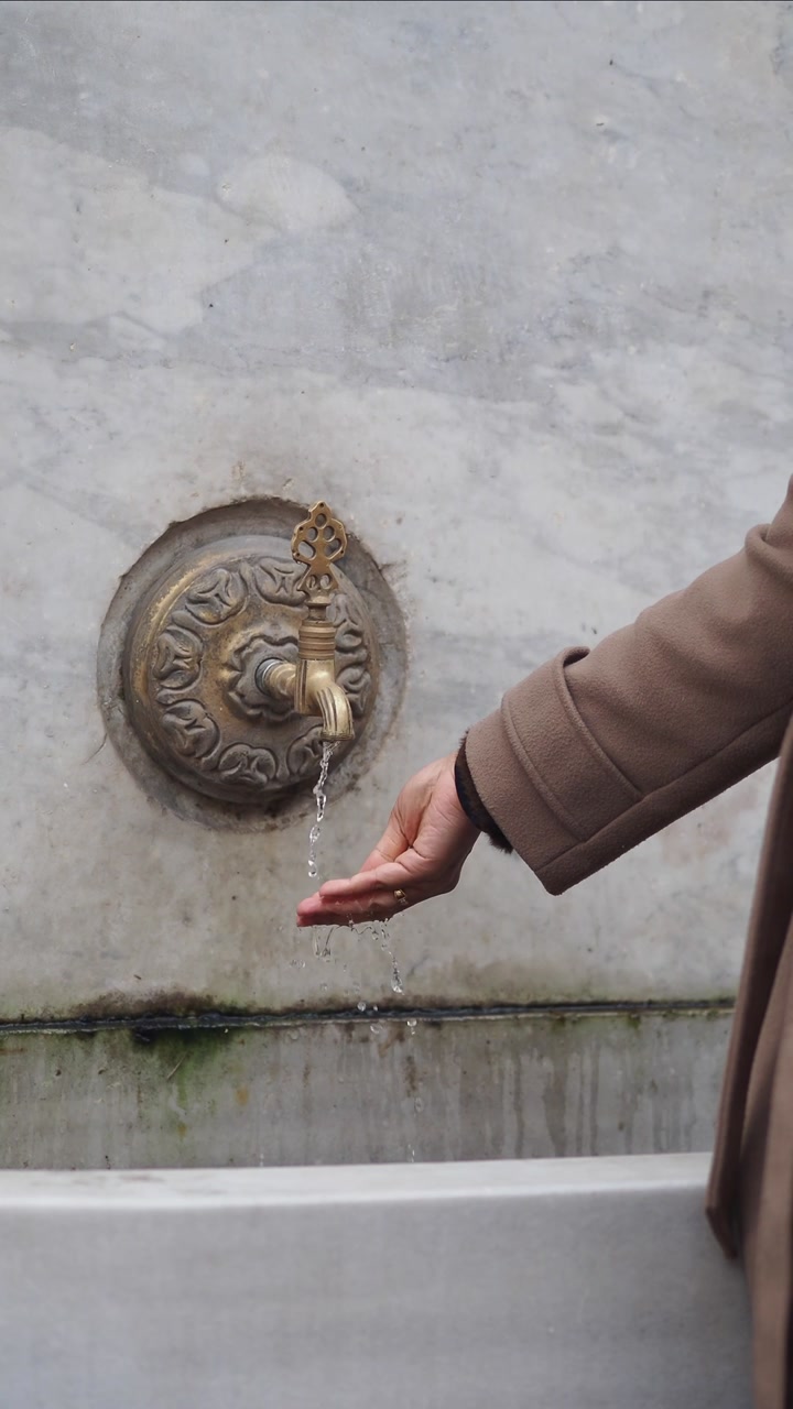 Person's Hand Catching Dripping Water from an Old Brass Faucet