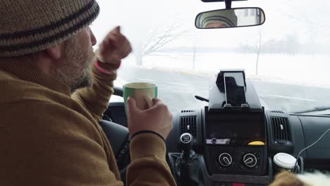 man drinking coffee or tea in camper van, sitting inside, having a rest after long journey, closeup view