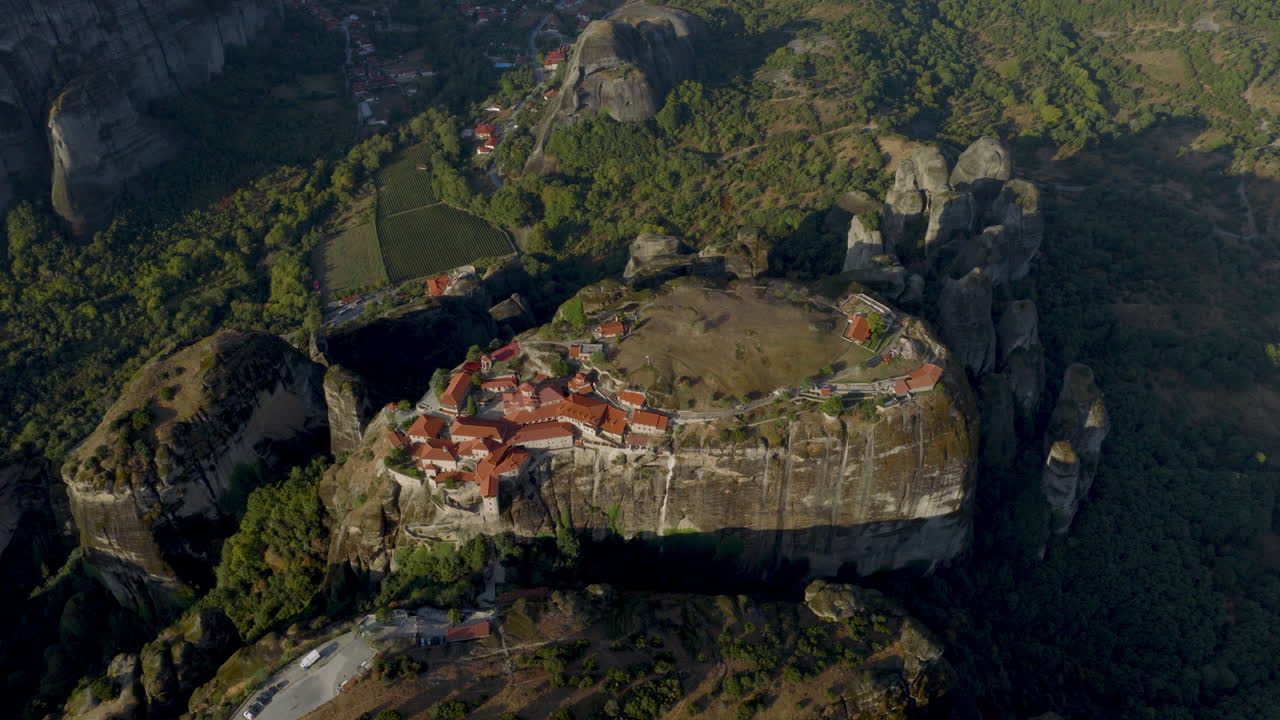 Cinematic aerial view of Meteora monastery in Greece perched on towering cliffs, dramatic rock formations and lush green valley create a breathtaking historic scene