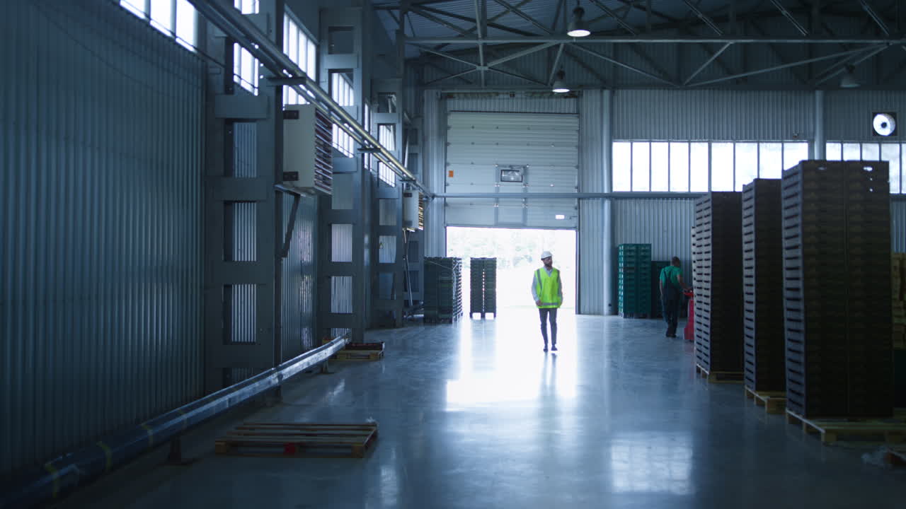 Dipendente di fabbrica che cammina, controllando i pallet di consegna della produzione in magazzino.