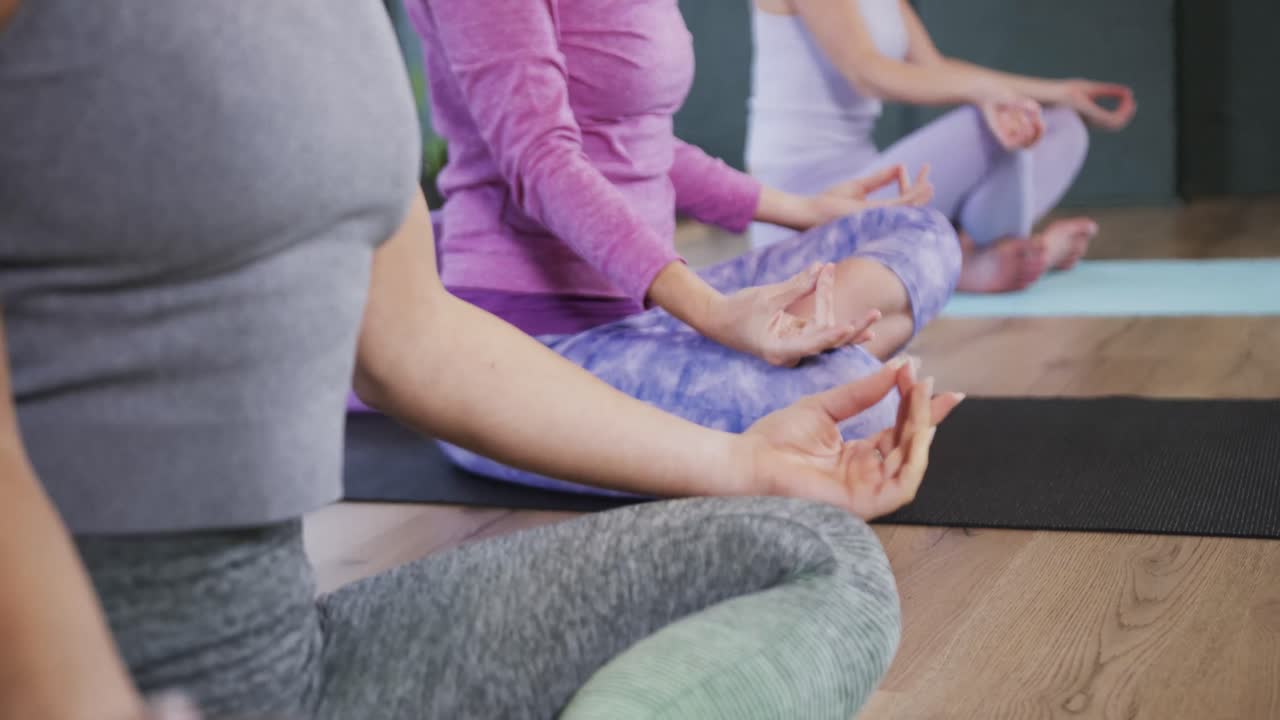 sección baja de mujeres diversas enfocadas meditando juntas en esteras en clase de yoga, cámara lenta