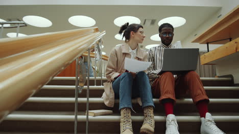 uomo e donna diversi che discutono di un progetto sul portatile in biblioteca