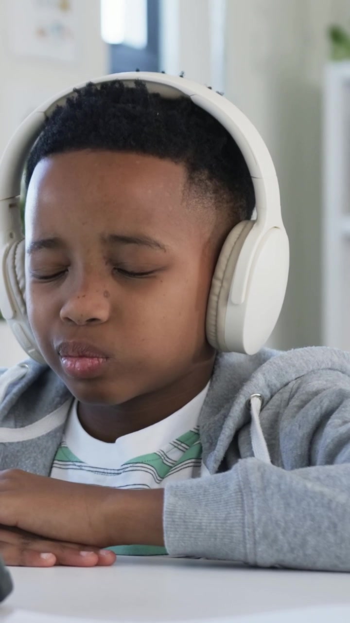 Video verticale: Audio in riproduzione, ragazzo con felpa grigia che canta e poi ascolta a casa con cuffie e tablet.