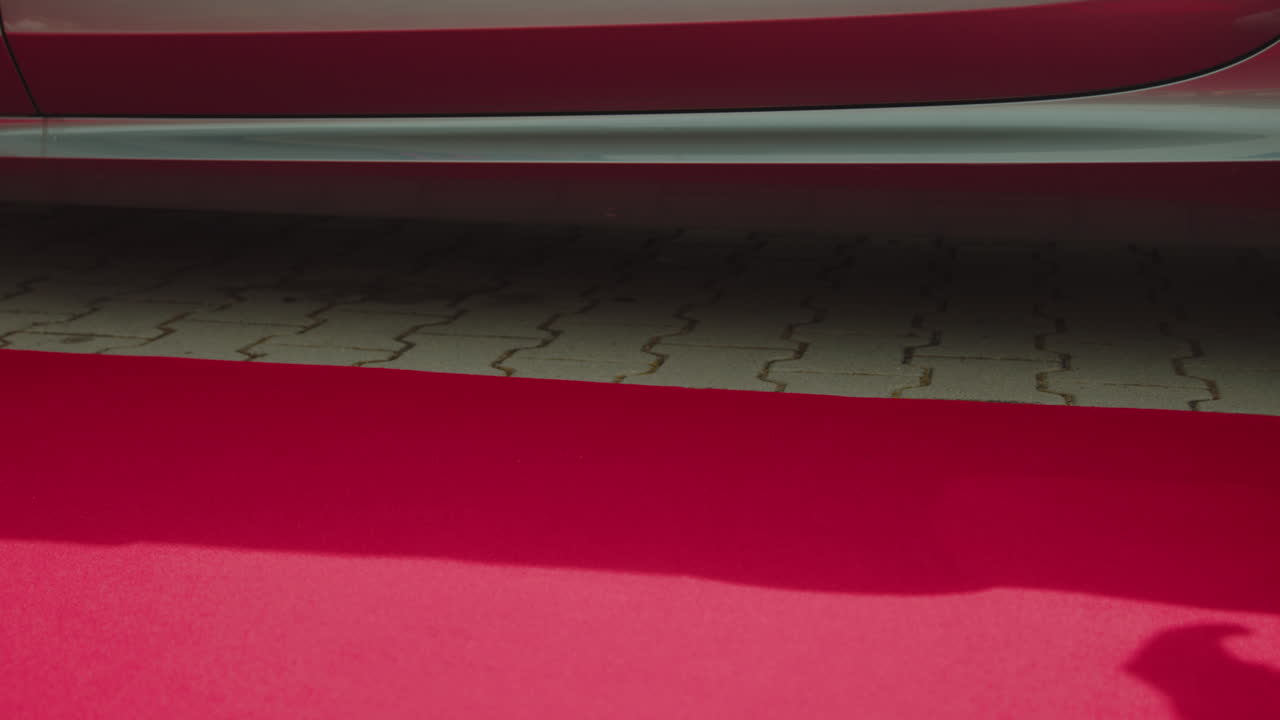 흰색 신발을 신은 남자가 문을 다시 닫기 전에 하차하는 빨간색과 광택이 나는 자동차의 문을 엽니다