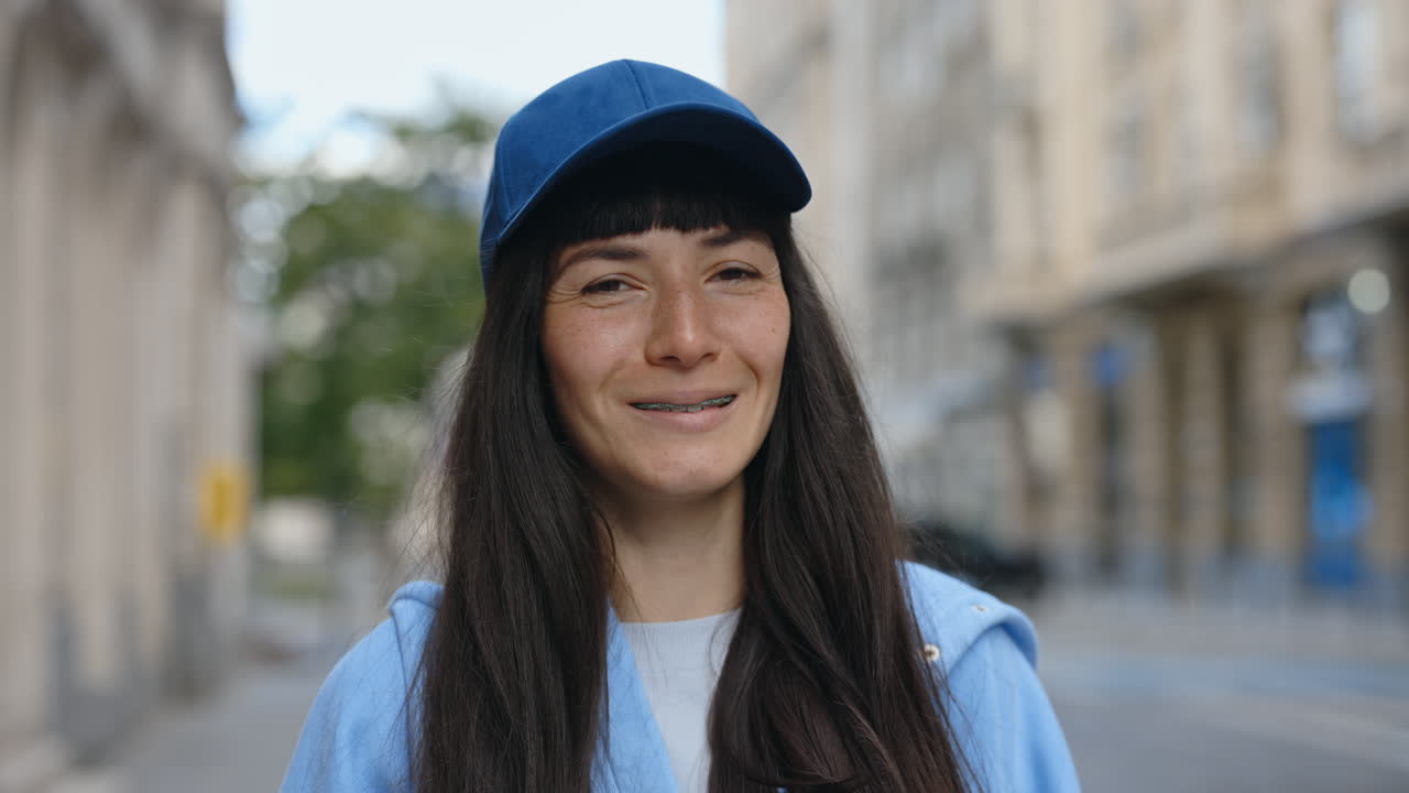 Portrait of a woman with braces and a baseball cap on a city street