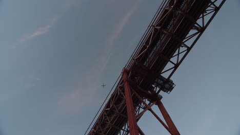underneath the 25 de abril bridge in lisbon, portugal (it´s a golden bridge, san francisco lookalike). shot during magic hour. an airplane travels across the sky