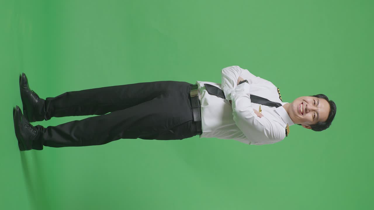 모습으로 가득 찬 몸 아시아 남성 조종사가 미소 짓고 녹색 스크린 배경 스튜디오에 서 있는 동안 카메라에 팔을 고 있습니다.