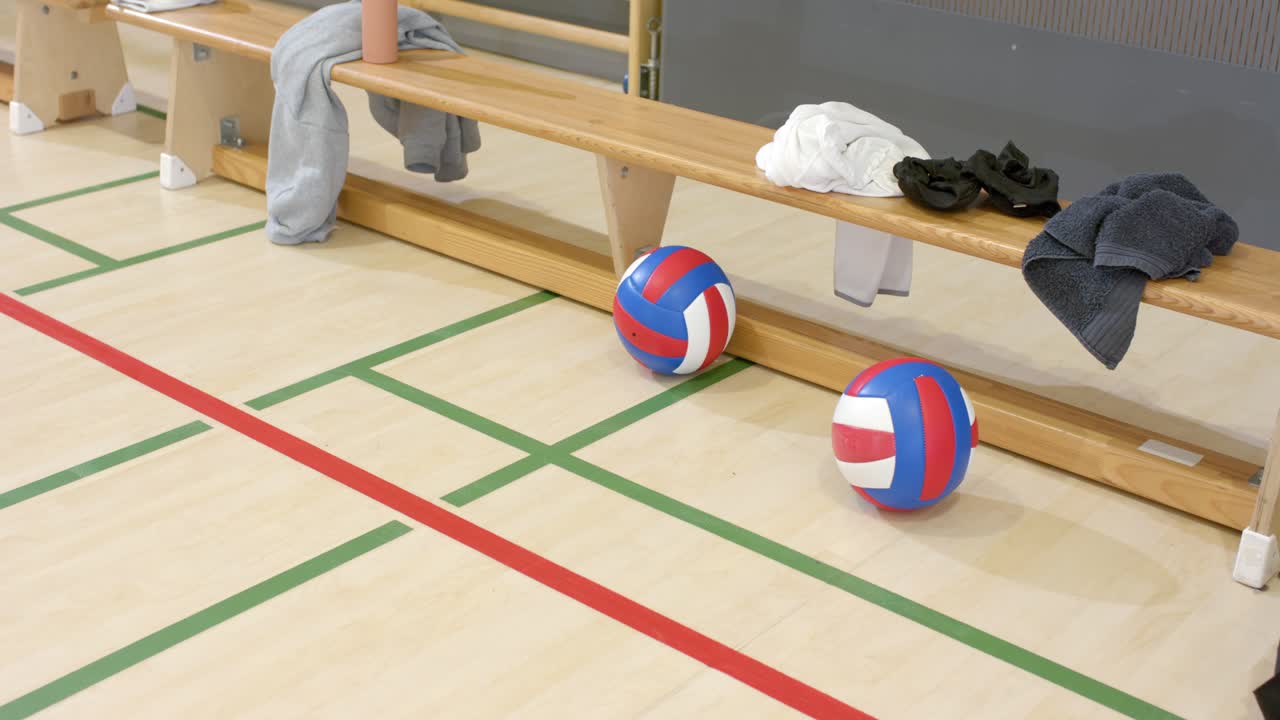 Når kameraet starter, ligger to volleyballer på banegulvet ved benken, i påvente av trening.