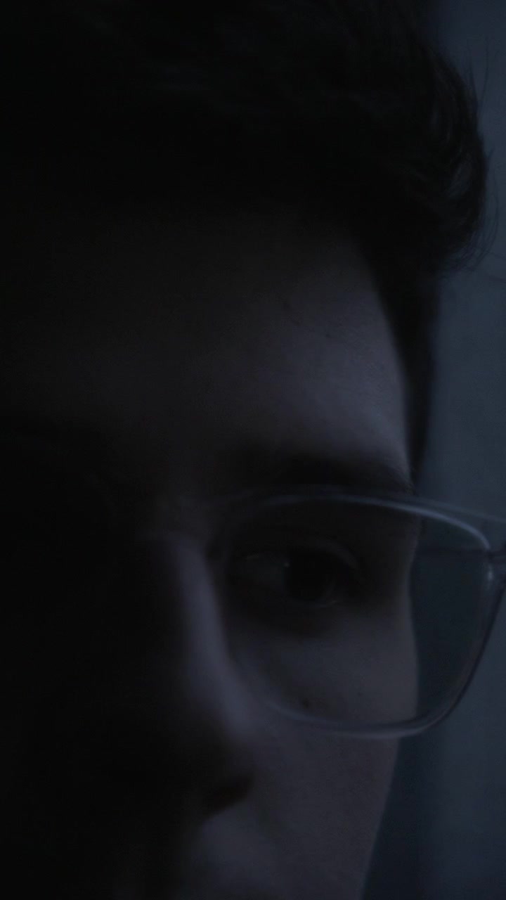Extreme close-up of a man's face with glasses in the dark storm looking with curiosity as lightning flashes