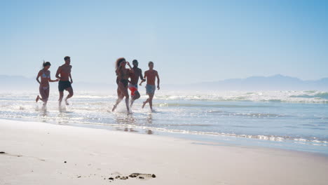 Gruppe-Von-Freunden,-Die-Im-Strandurlaub-Durch-Wellen-Laufen