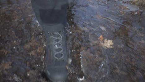 a person wearing a black boots stepping into the watery ground with fallen leaves