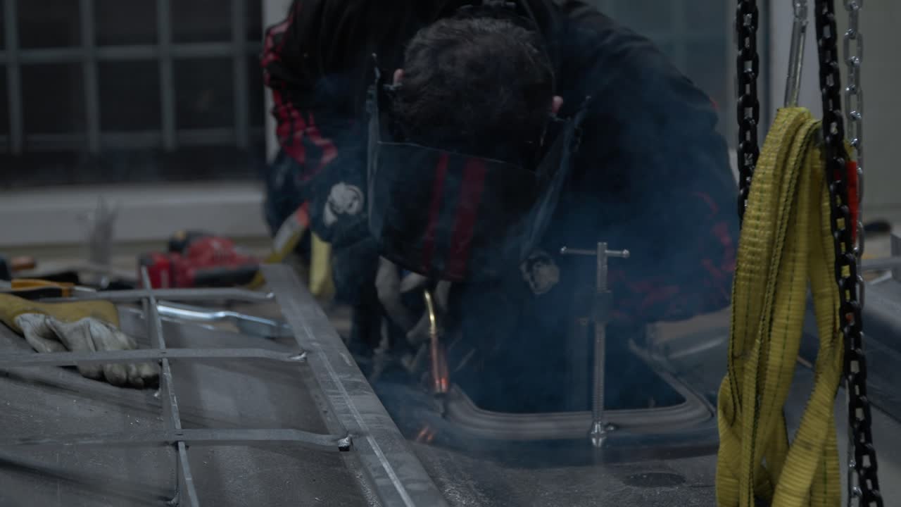 용접공의 헬멧 가스 용접 알루미늄 금속 부품, 차고에 지어진 수제 보트 - 슬로우 모션 중간 샷