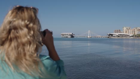 woman taking pictures of ventus harbor hotel and pista e re bridge in durres, albania. - wide shot
