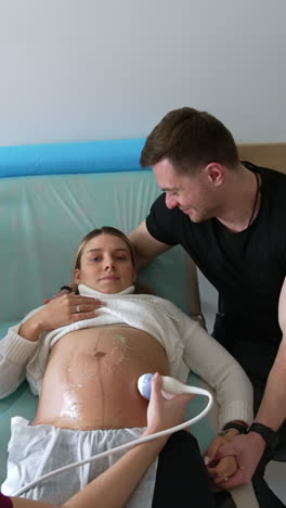 husband supporting his pregnant child at doctor's examination. doctor performs the ultrasound check for expecting mom. vertical video