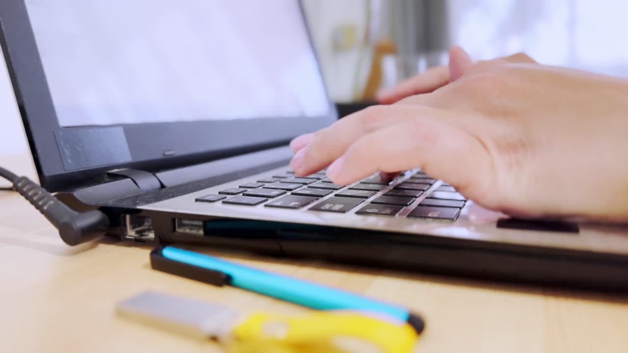 Close-up from the side, focusing on a laptop keyboard and female hands actively typing.