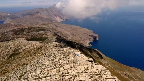 Toma-Aérea-De-Grecia-En-Un-Pico-Rocoso-Con-Una-Pequeña-Casa-Blanca,-Amorgos