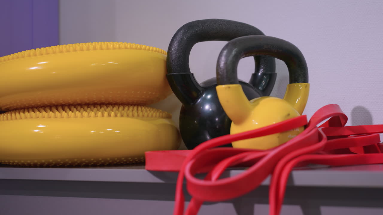 Close-up of various gym equipment, including kettlebells, resistance bands, and balance discs, neatly arranged on a shelf for strength training, functional workouts