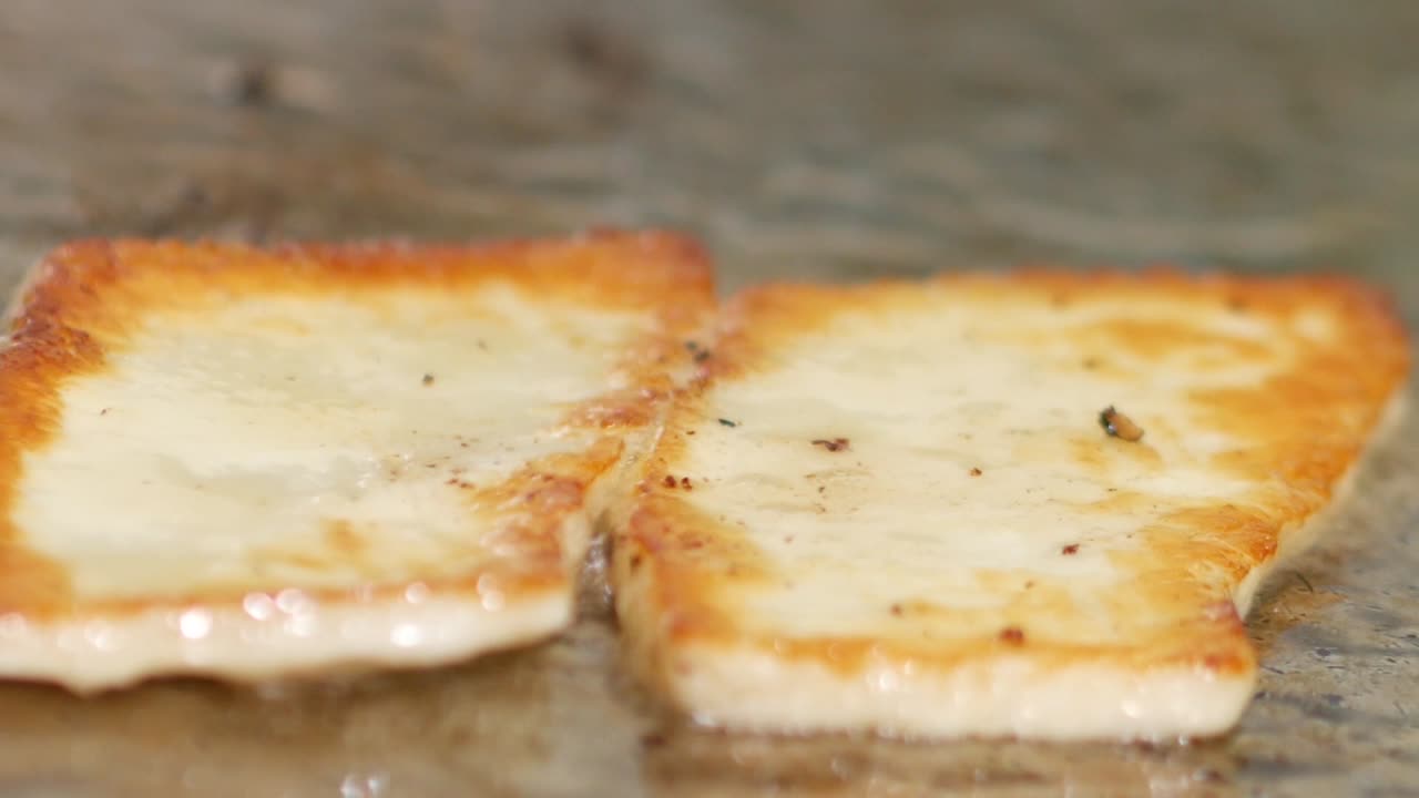 Close-up of halloumi cheese sizzling on a grill and flipped with a spatula after being browned