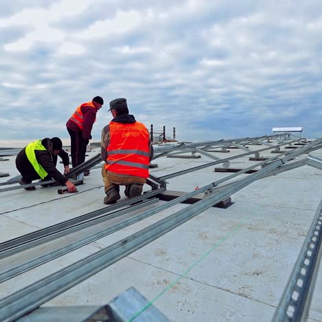 solar panel technicians on flat roof of a big building. metal base before the construction of photovoltaic panels. workers installing new solar farm.