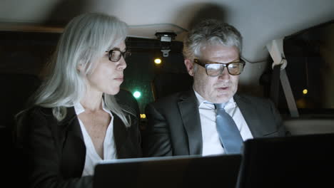 business partners using laptops in car at night