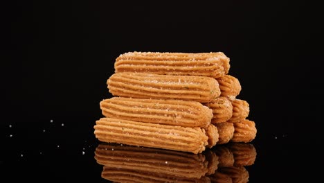 a neatly stacked pile of churros rotates and zooms out against a glossy black background, with dramatic studio lighting and crisp reflections