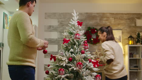 una pareja con ropa a juego decora su árbol de navidad