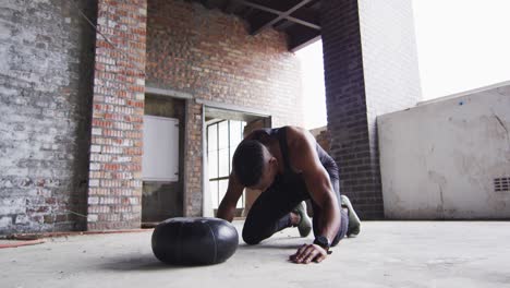 hombre afroamericano descansando después de hacer ejercicio con una pelota de medicina en un edificio urbano vacío