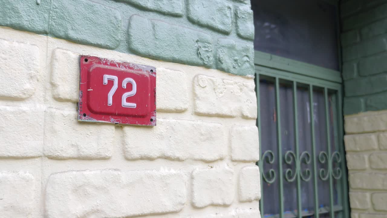 House number 72 on brick wall with security bars