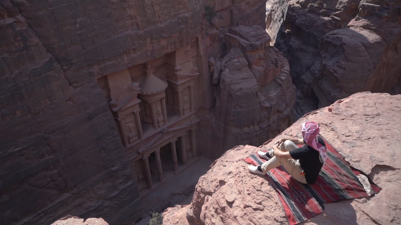 hombre sentado en el mirador del acantilado sobre el templo de petra, jordania