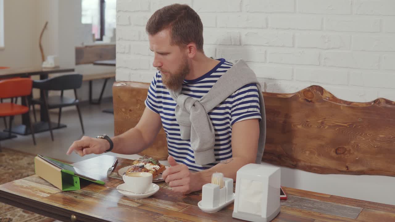 hombre comiendo el desayuno en un café con una tableta