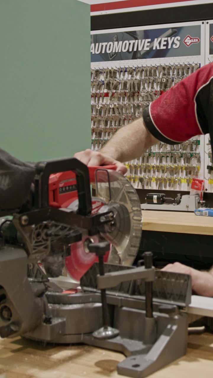 Vertical close-up of a technician using a bench-mounted mitre saw to cut a metal frame. The circular blade spins as the material is guided into position, capturing precision cutting