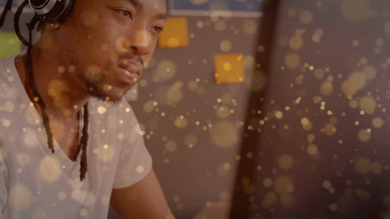 Man adjusting headphones at desk, camera panning up revealing sticky notes and gold bokeh for tech