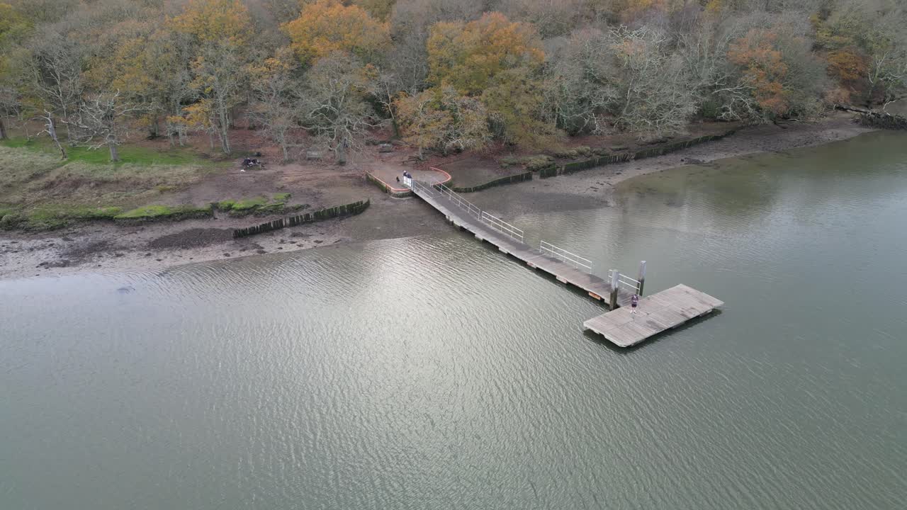 Aerial view showing Manor Farm pontoon stretching into calm Hamble River with soft ripples on water, muddy banks, and autumn woodland creating quiet rural setting in Hampshire under daylight
