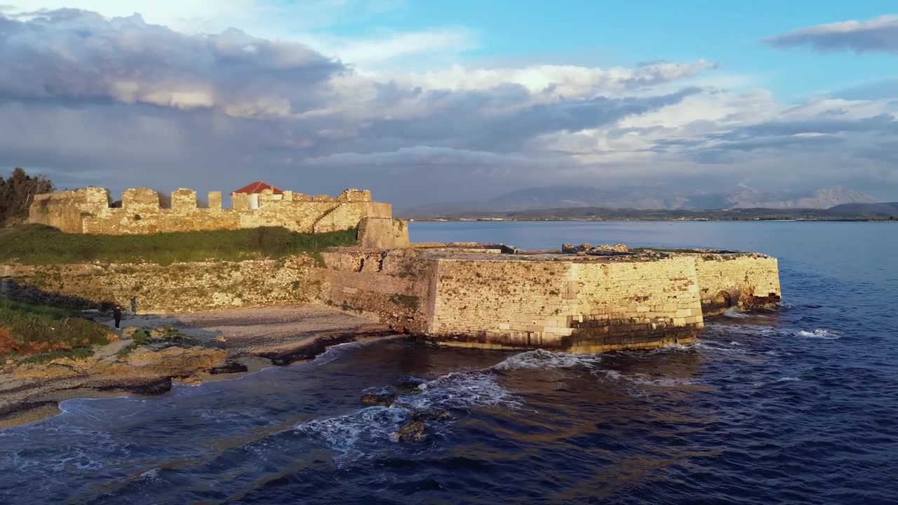 Epica ripresa aerea in 4K con drone che si allontana, partendo da una finestra di una storica fortezza in pietra, rivelando il massiccio Castello di Pantokrator e lo splendido orizzonte marino al tramonto a Preveza, Grecia.