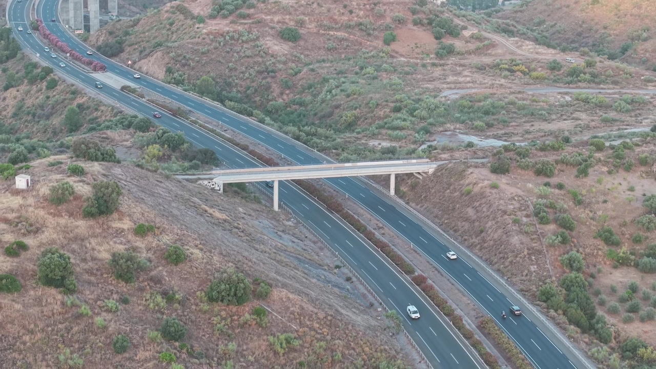 Vista da drone in lontananza di un'autostrada regionale a più corsie che attraversa colline aride e un paesaggio rurale aspro con infrastrutture a ponte, Malaga, Andalusia, Spagna