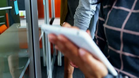 sección media de una mujer usando una tableta digital mientras sus colegas discuten sobre notas adhesivas