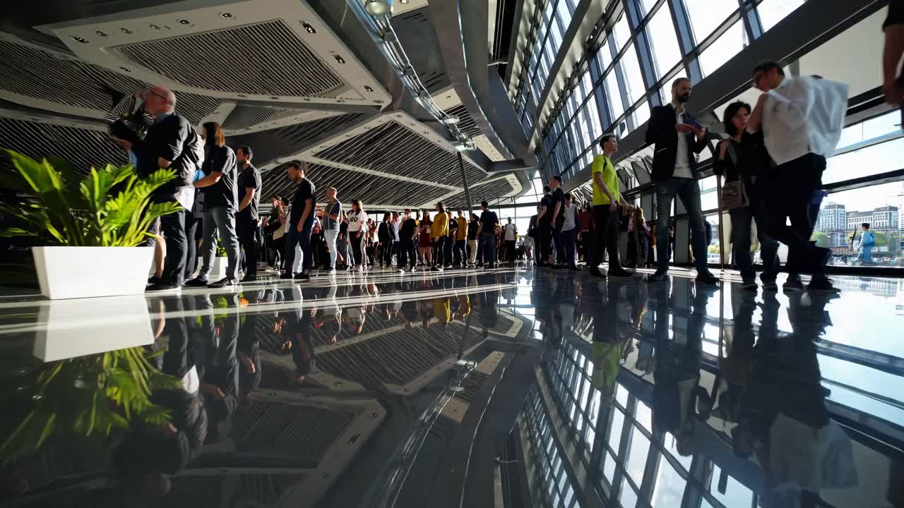 Wide-angle video capturing a bustling crowd in a modern atrium, with reflections on the shiny floor
