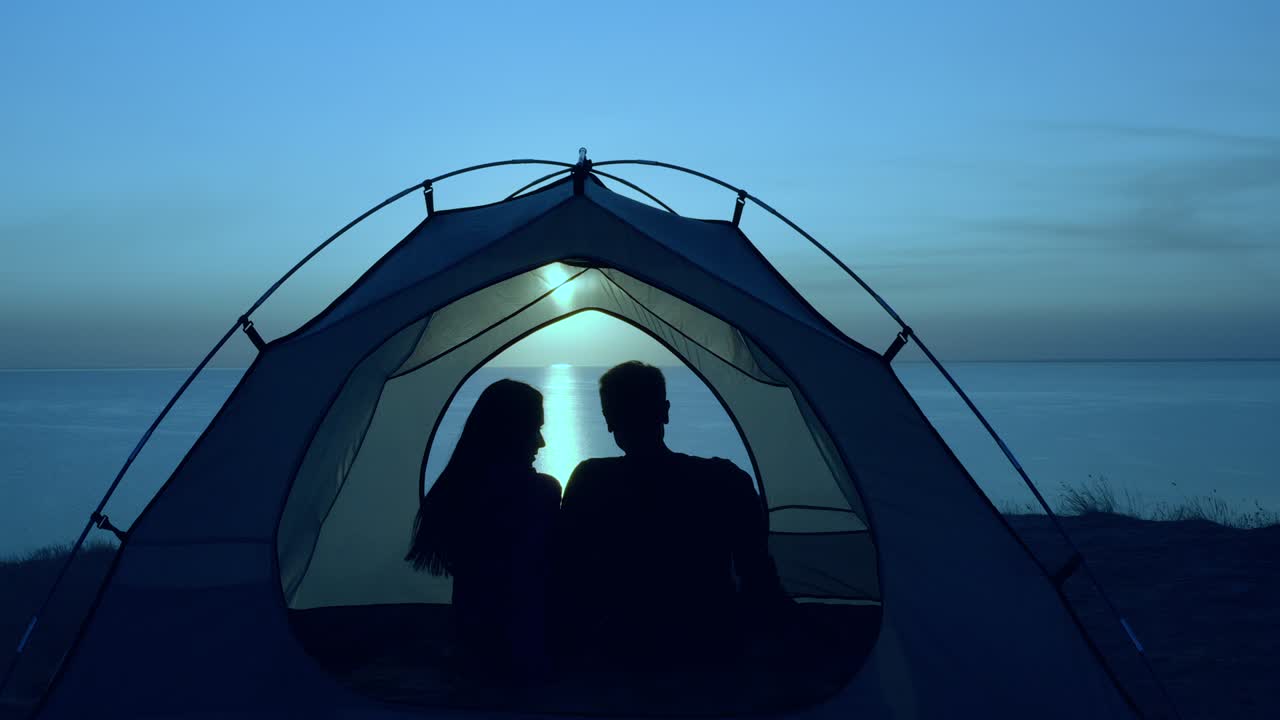 로맨틱한 커플이 밤의 바다 풍경에 맞춰 텐트에 앉아 있습니다.
