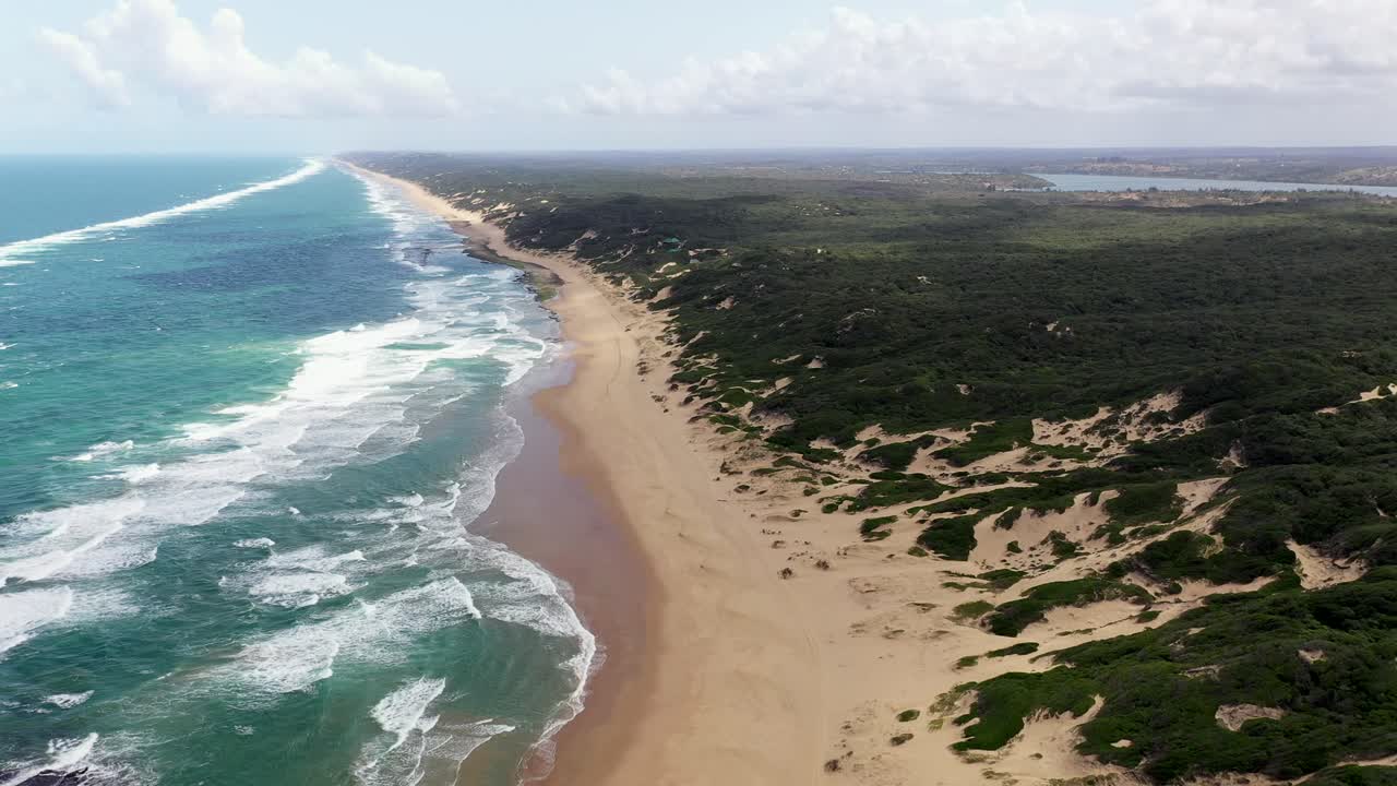 Tomada aérea frontal de alta altitude da Praia de Chidenguele, em Moçambique, com o Lago Inhampavala ao fundo.
