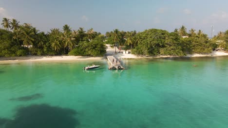 flight over the turquoise water surface towards the beger on which green trees grow past the pier to which the boat is moored