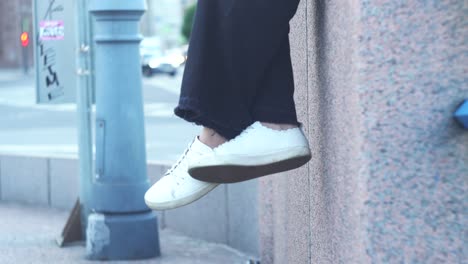 woman's legs and shoes hanging off a city wall