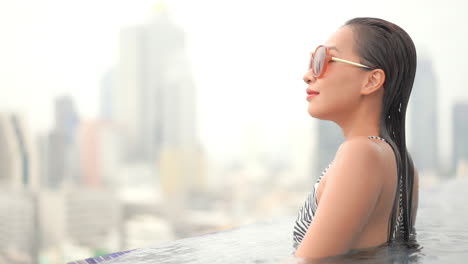 young classy asian woman in rooftop infinity pool with stunning urban city view