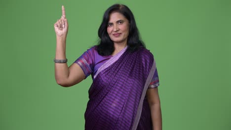mature beautiful indian woman pointing up while wearing sari traditional clothes