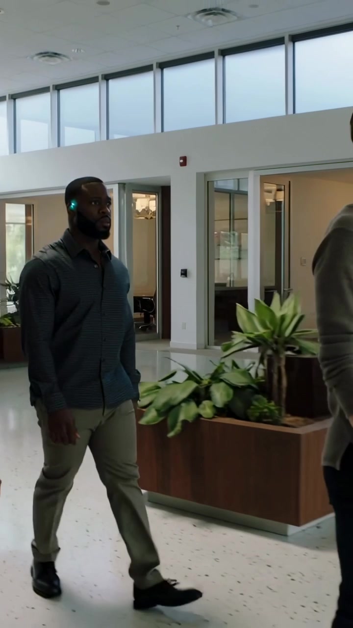Vertical video: Entering left, man wearing dark shirt khakis walking across lobby glowing earbud