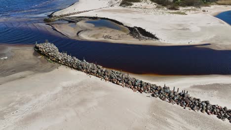 On-the-bed-of-the-Holy-river-flowing-into-the-Baltic-Sea,-on-the-left-bank,-stones-are-laid-along-the-remains-of-an-old-bridge-on-the-beach